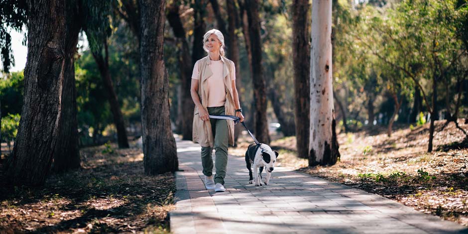 Mujer adulta paseando en medio de un parque en compañía de su mascota blanco con negro. Aprende cuánto vive un perro y disfruta más con él.