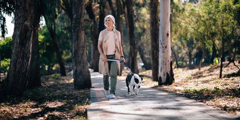 :  Hay beneficios en el cuerpo de un tutor al tener un perro. Mujer paseando a su mascota.